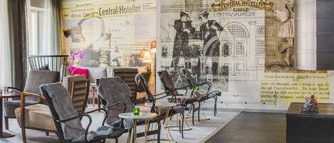 A hotel lobby with modern furniture, a large historical mural, and a seating area with tables and chairs.
