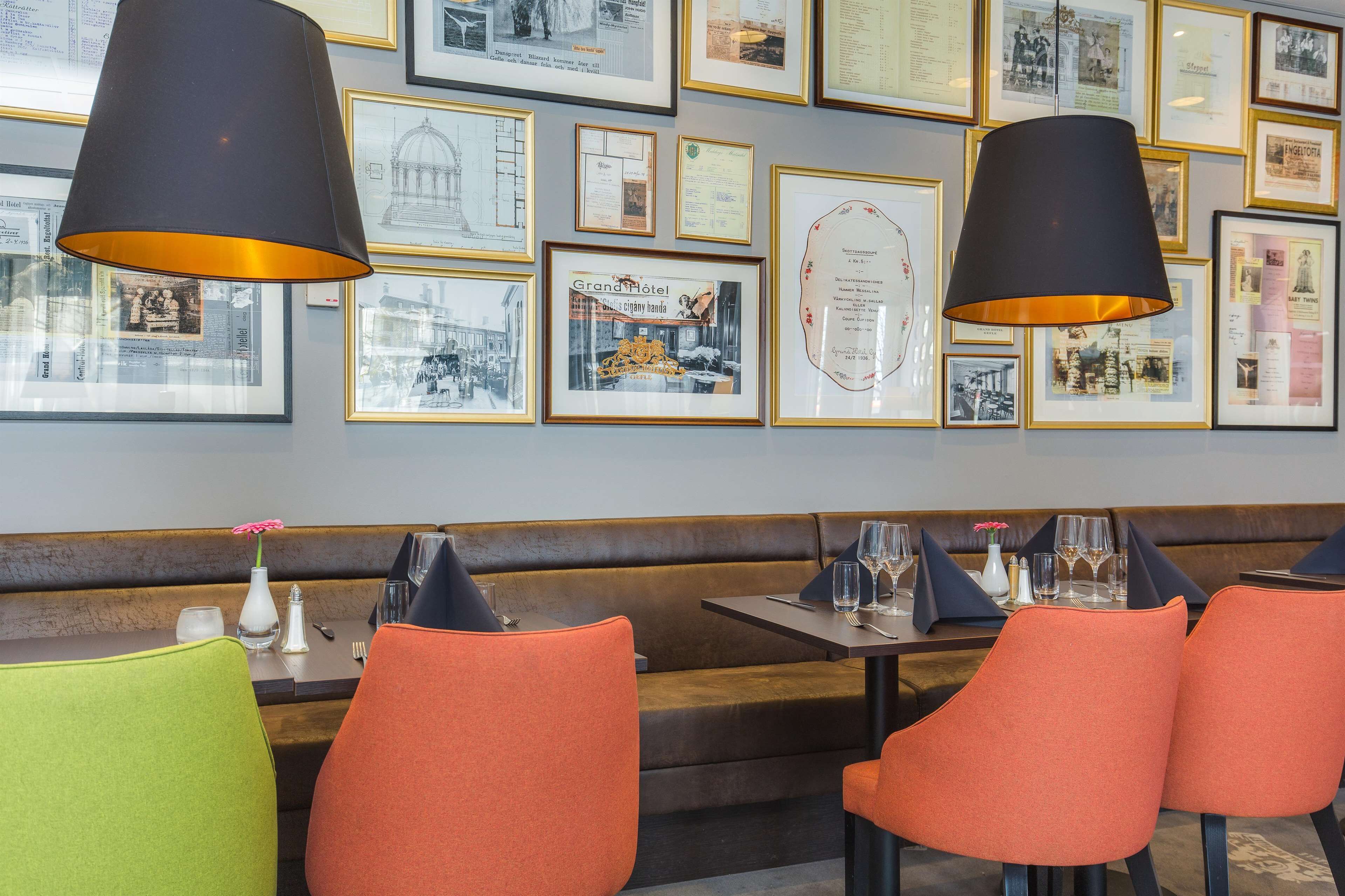 A restaurant interior with a long counter, orange and green upholstered chairs, black and gold framed photographs on the wall, and black pendant lighting.