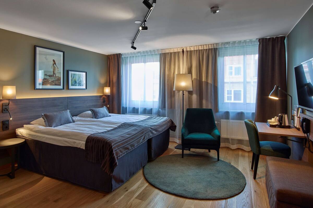 Una habitación de hotel con una cama grande, un escritorio con silla, televisión y una lámpara.