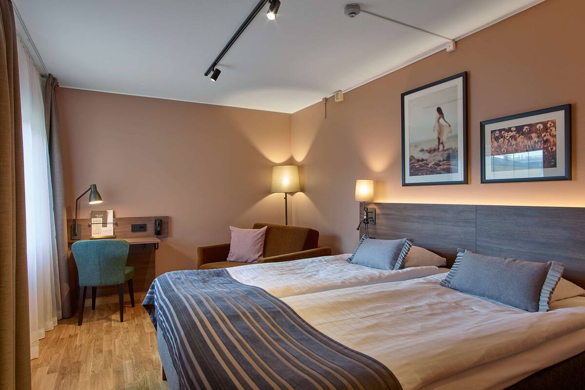 Habitación de hotel con dos camas, un escritorio, una silla y dos lámparas.