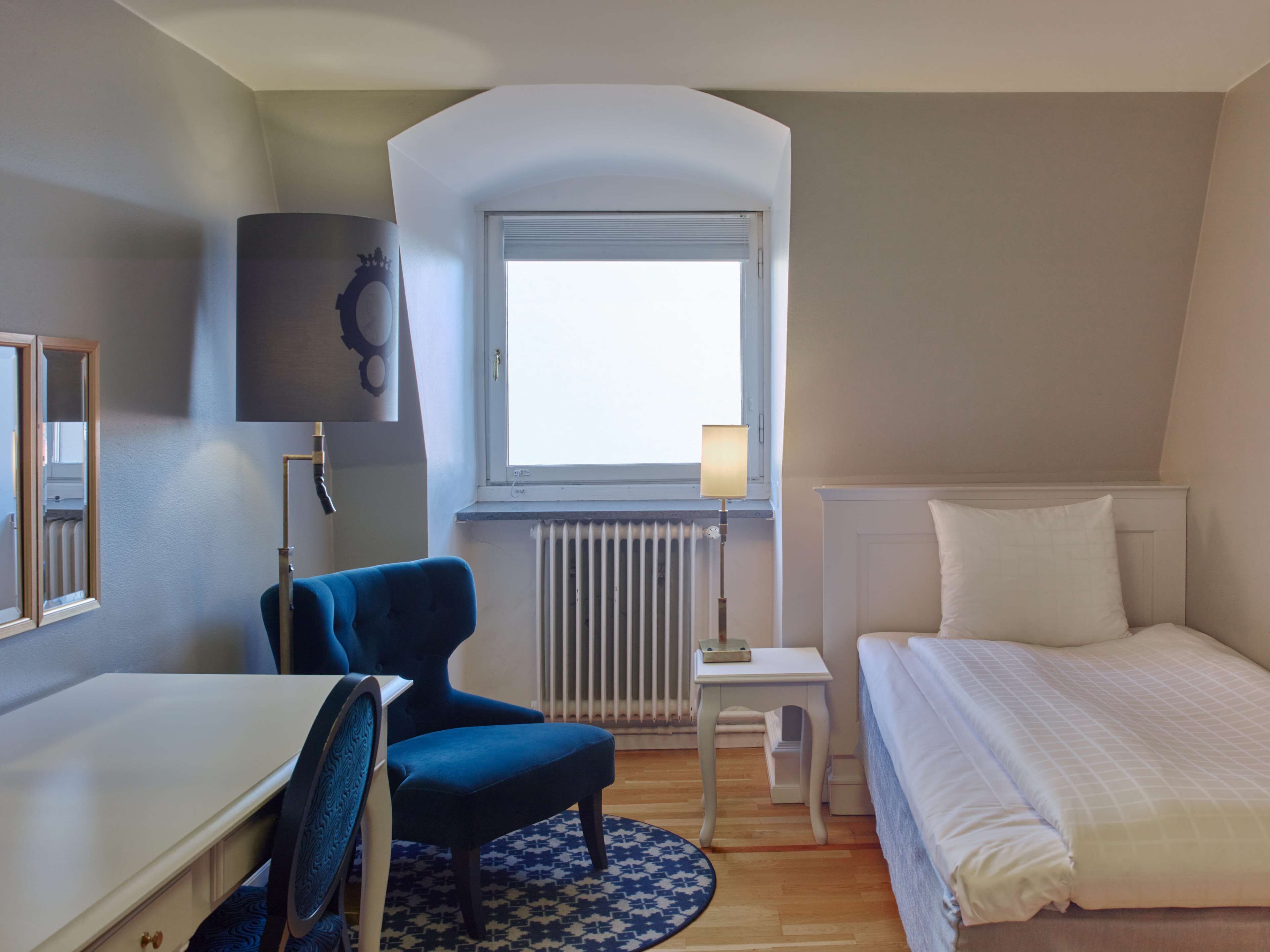 Un dormitorio con cama, escritorio, silla, ventana y radiador.