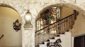 Una imponente escalera con barandillas ornamentadas, una escultura de caballo y un vitral.