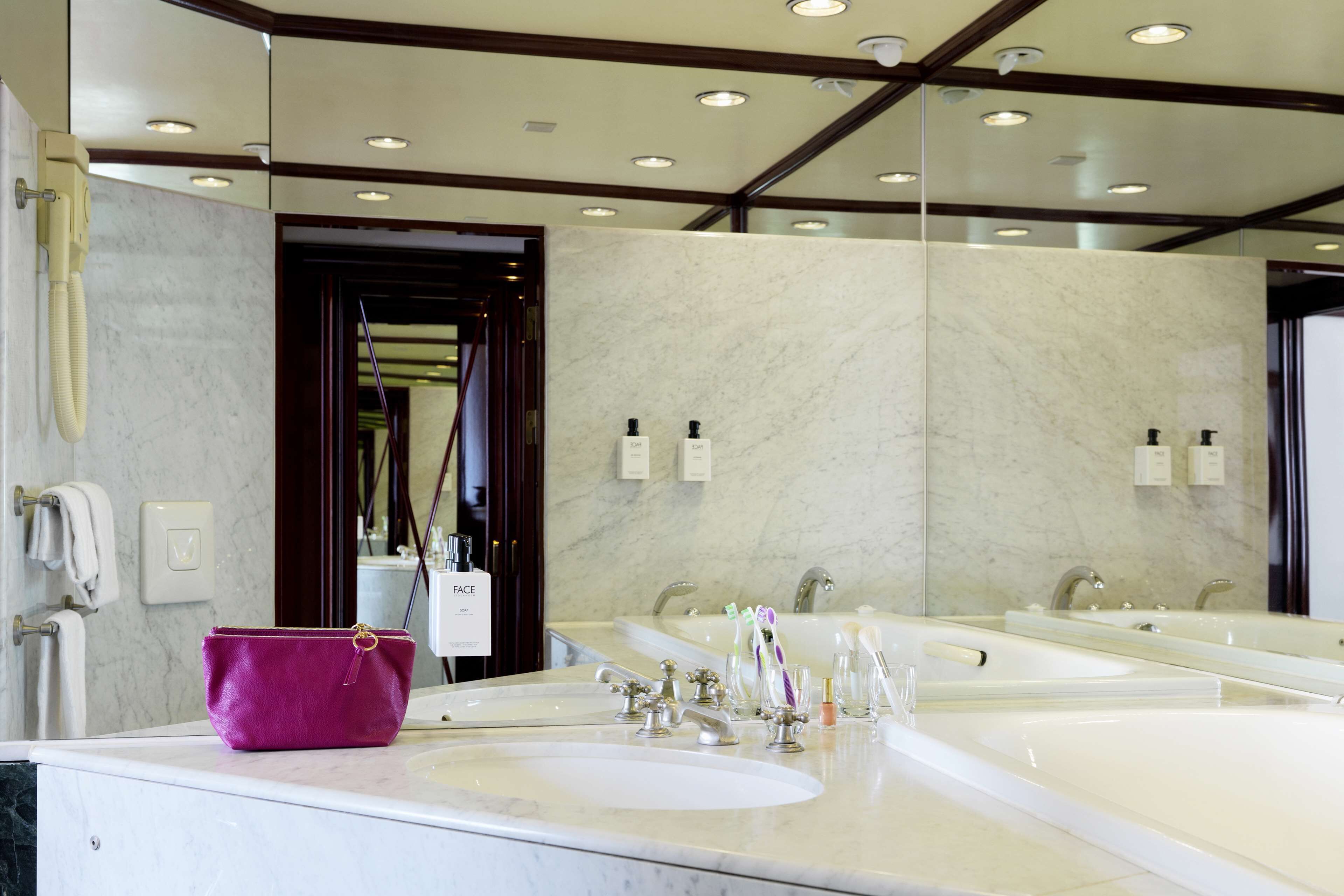 A hotel bathroom with a large mirror, two sinks, and a vanity area.