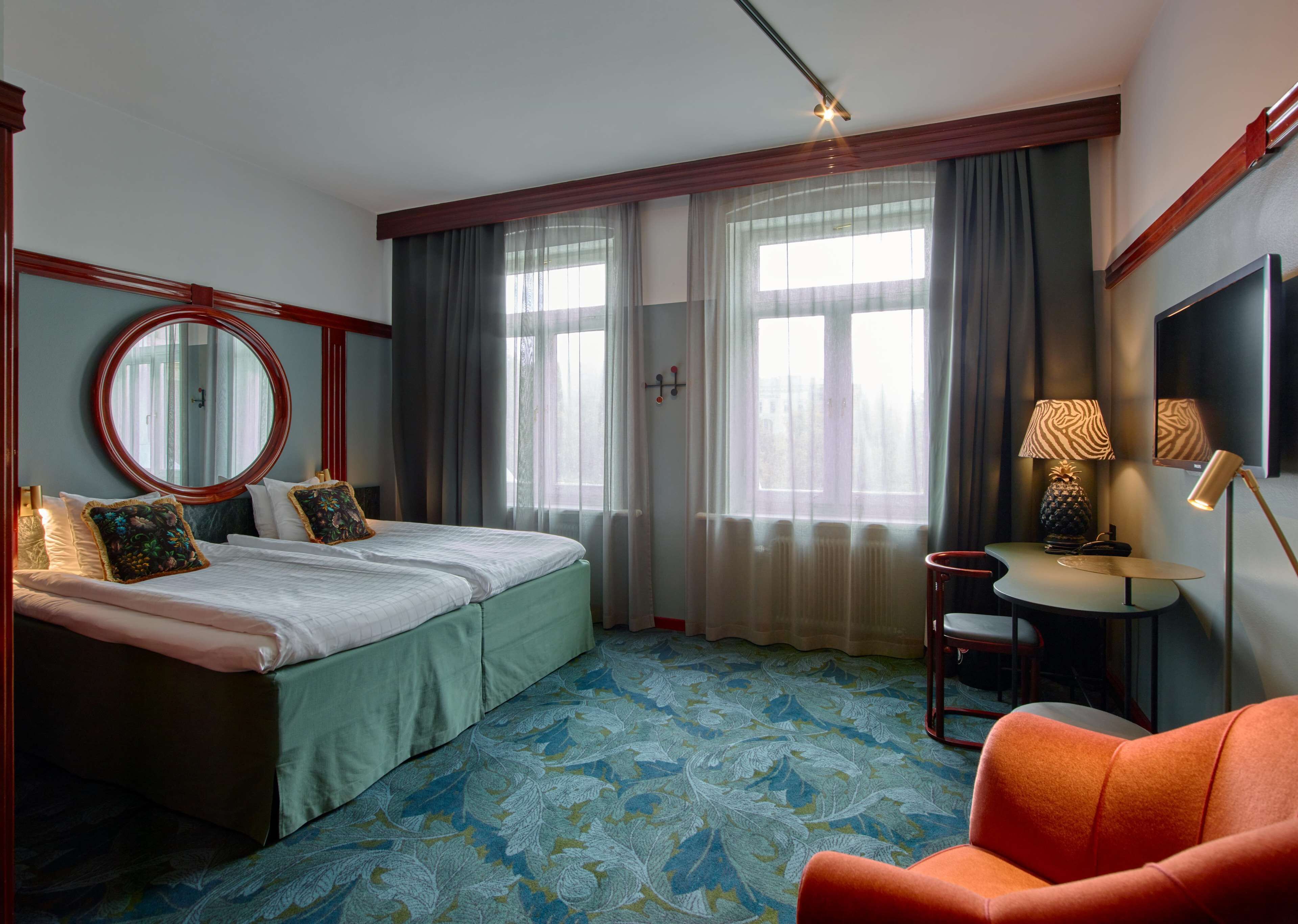 Et hotelværelse med en dobbeltseng, et rundt spejl, et lille bord med en lampe og en stol.