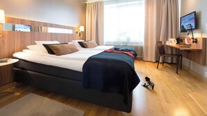 Una habitación de hotel con una cama grande, un escritorio con silla, televisión y ventana con cortinas.