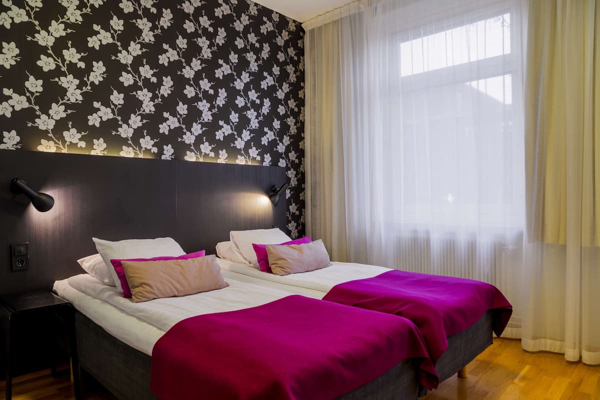 Una cama doble con ropa de cama blanca y rosa, un cabecero oscuro y una pared con estampado floral.