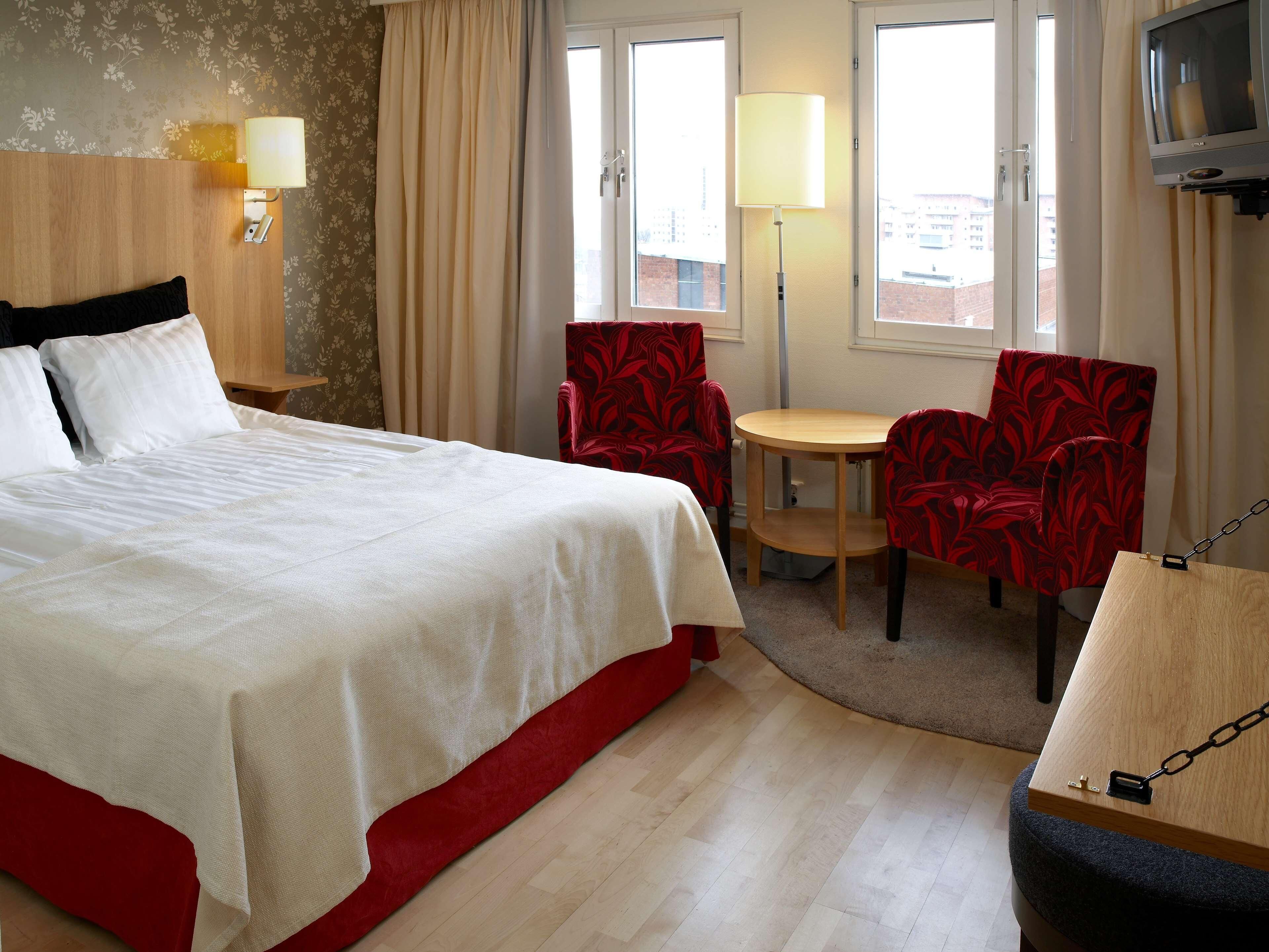 Habitación de hotel con cama, una mesa, dos sillas, televisión y ventana con cortinas.