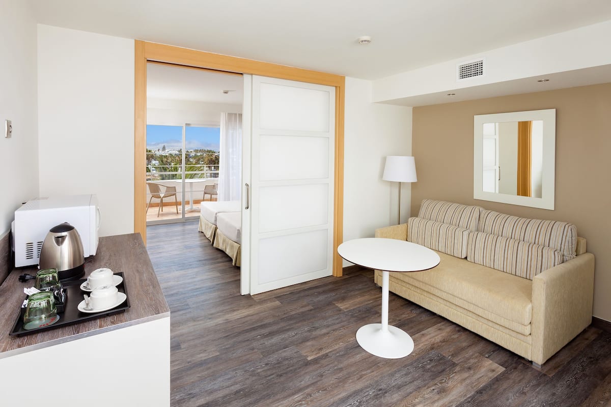 A hotel room with a wooden floor, a beige sofa, a small white table, and a coffee maker on a tray.
