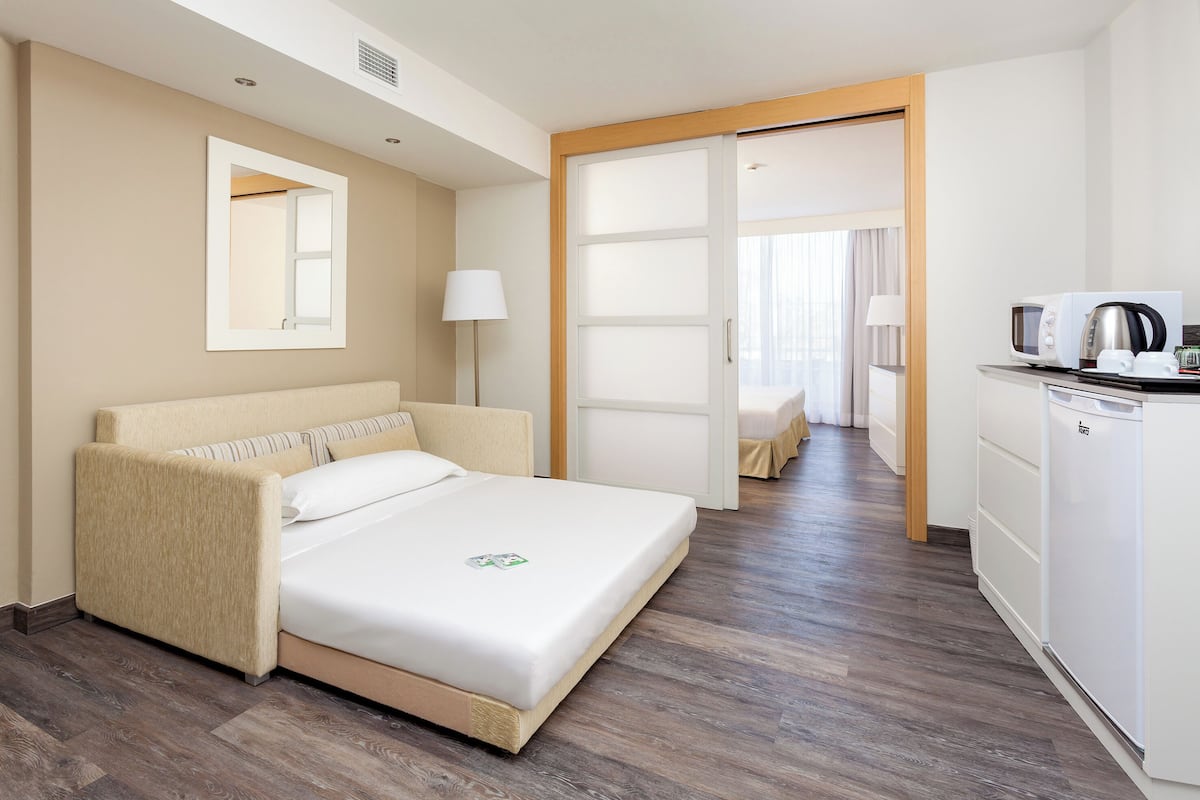 A hotel room with a bed, a desk with a microwave, a kettle, and a cabinet.