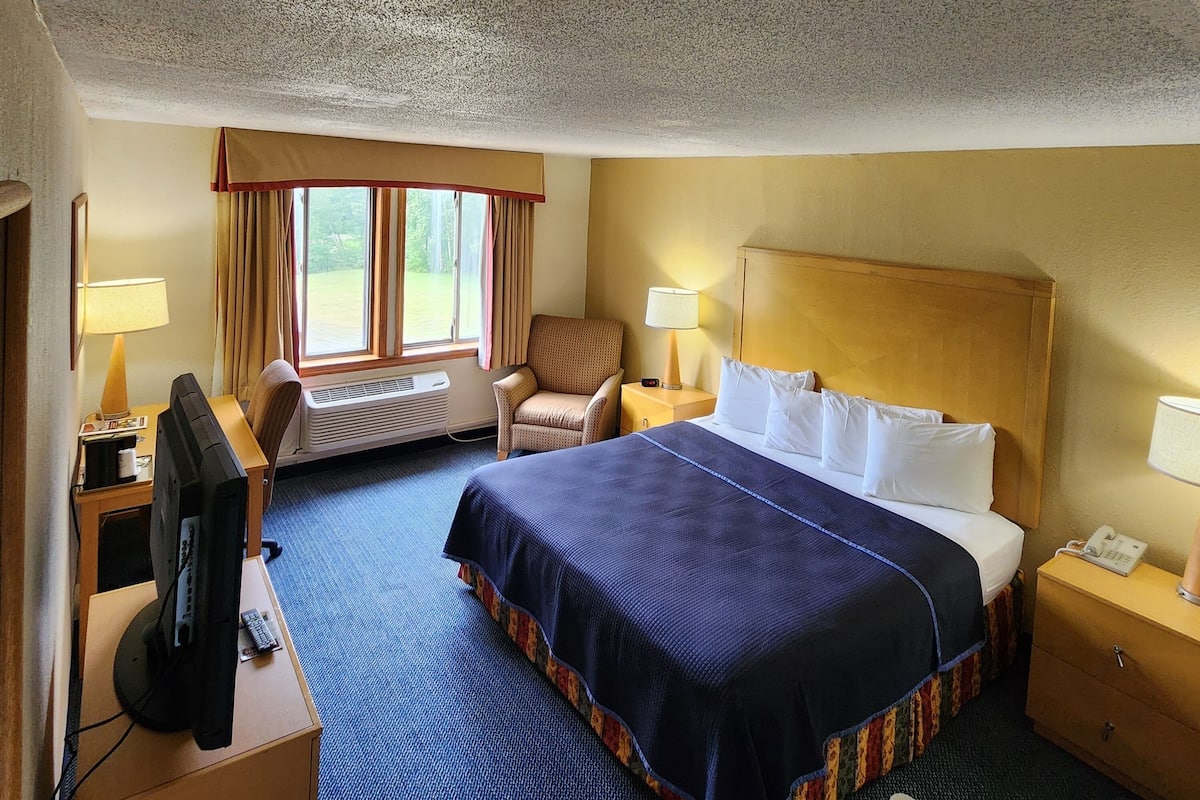A hotel room with a large bed, a desk with a computer, a chair, and a window with curtains.