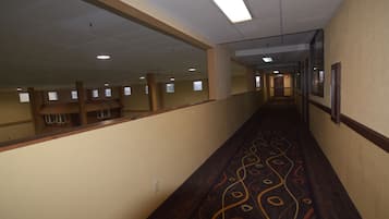 A long, narrow hallway with a patterned carpet, beige walls, and a ceiling with fluorescent lights.