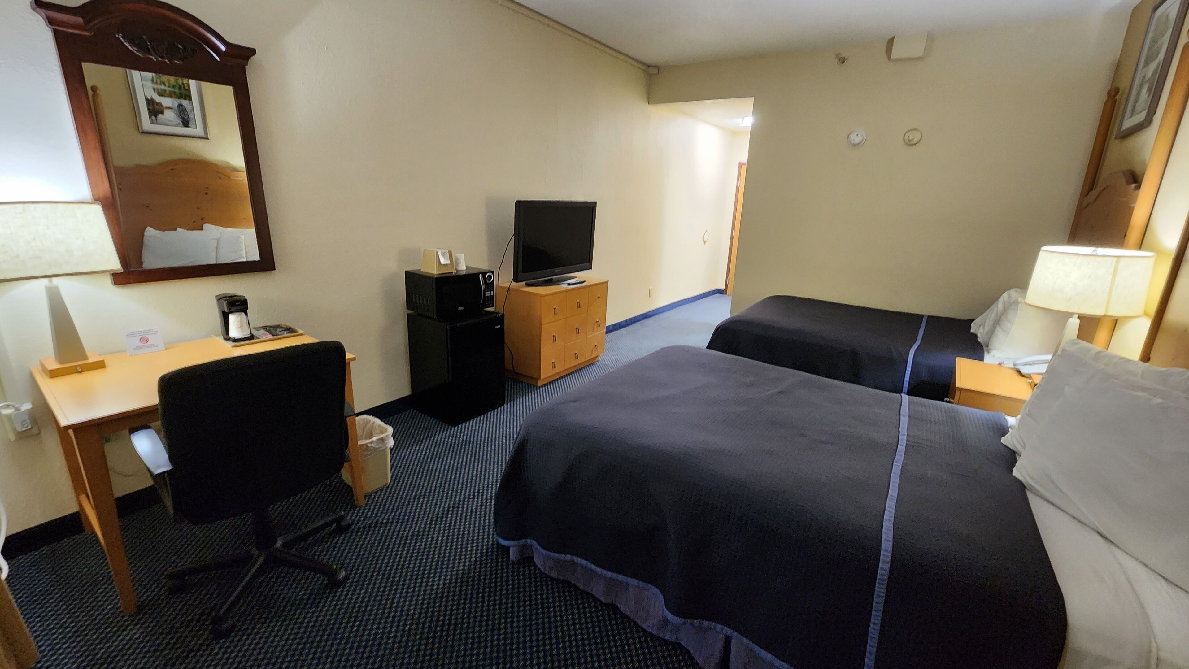 Habitación de hotel con dos camas, un escritorio con silla, televisor y un mueble bajo.