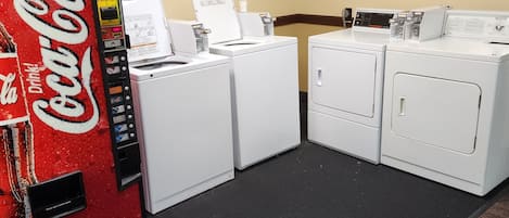 A laundromat with a Coca-Cola vending machine, multiple washers and dryers, and a carpeted floor.