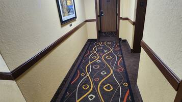 Un pasillo con alfombra estampada, un cuadro en la pared y una puerta al final.