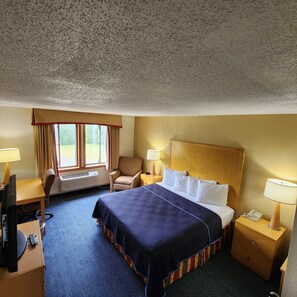 A hotel room with a bed, a desk, a chair, a lamp, and a telephone.