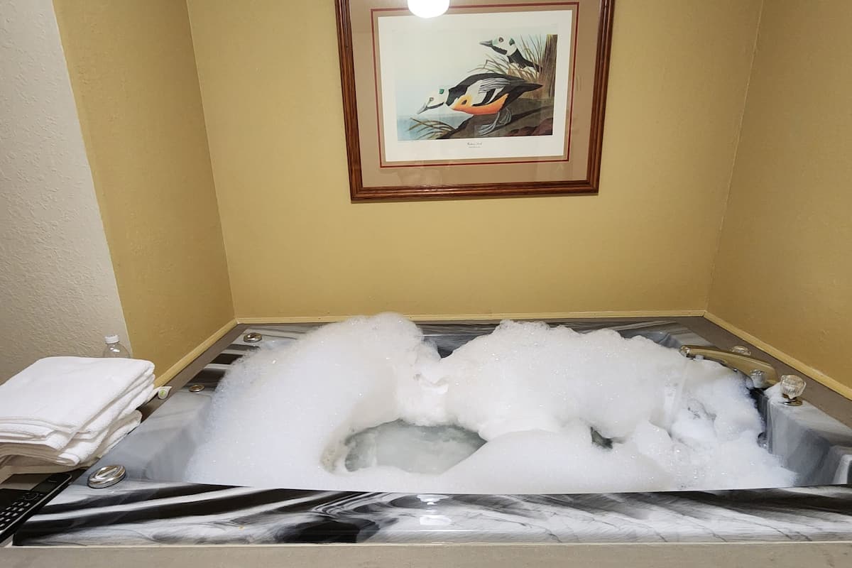 A bathtub filled with bubbles, a framed picture on the wall, and a stack of white towels on the side.