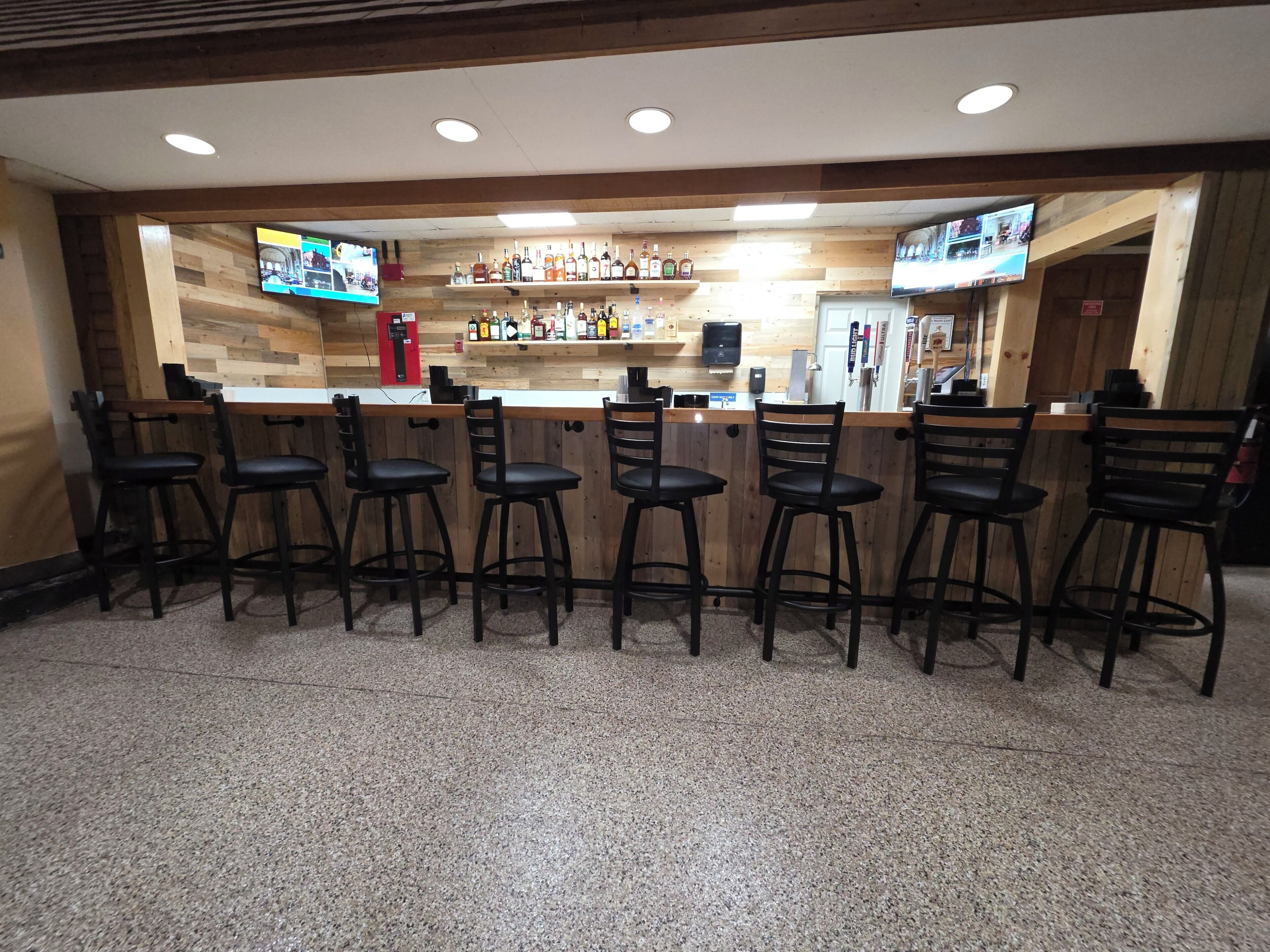 A bar area with wooden walls, multiple liquor bottles, and bar stools.