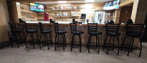 A bar area with wooden walls, multiple liquor bottles, and bar stools.