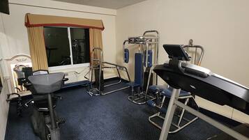 A hotel room with a treadmill, exercise equipment, and a window with curtains.
