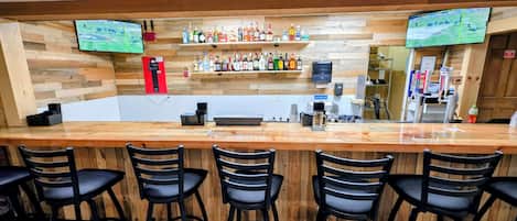 Un espace bar doté d’un comptoir en bois, de tabourets de bar et d’une étagère où sont exposées différentes bouteilles.