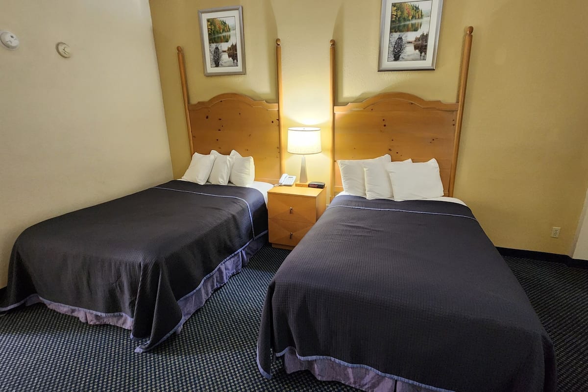 A hotel room with two beds, a nightstand with a lamp, and two framed pictures on the wall.