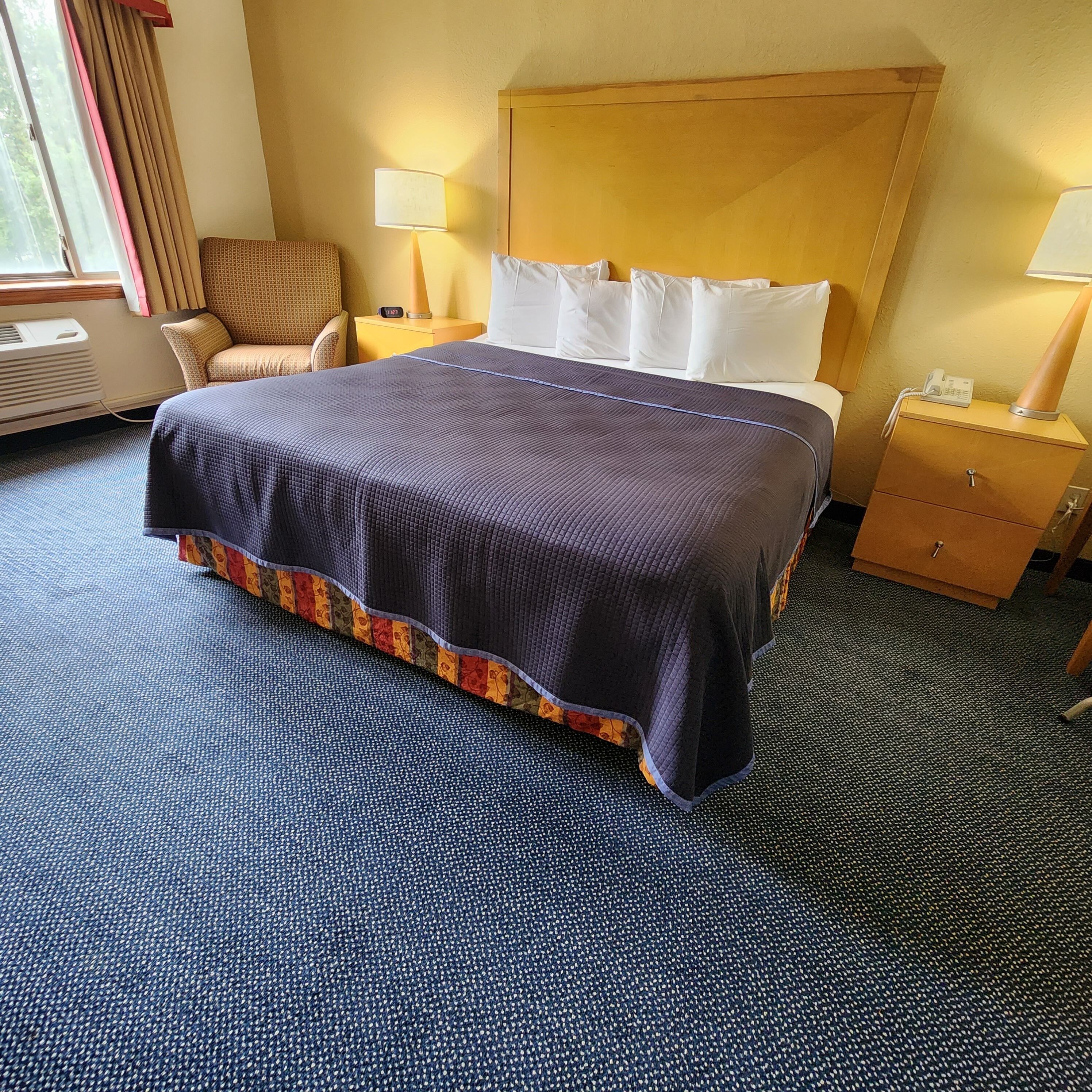 Una camera d'albergo con un letto grande, una sedia, un comodino con lampada e una testiera in legno.