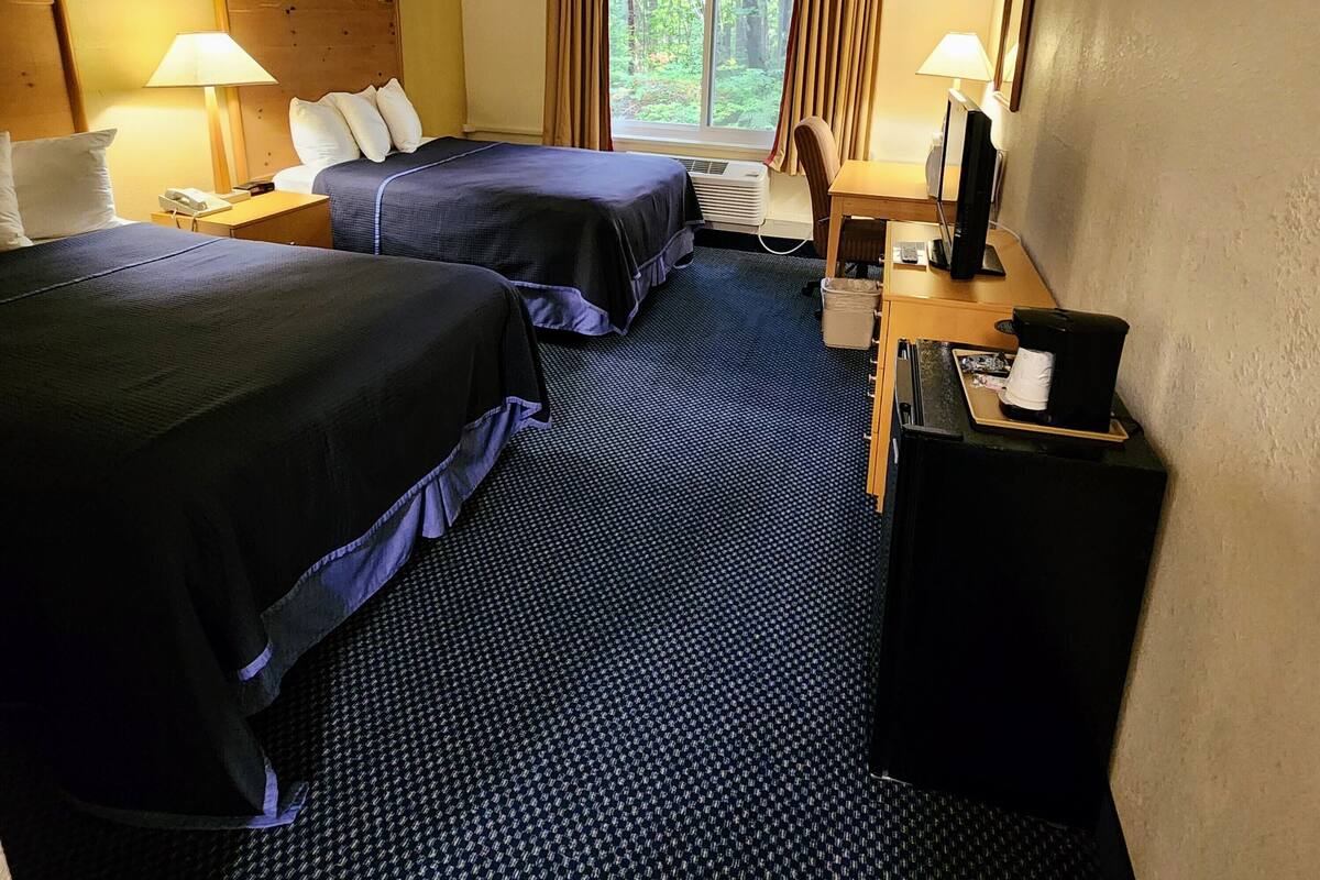 A hotel room with two beds, a desk with a computer, a telephone, and a window with curtains.