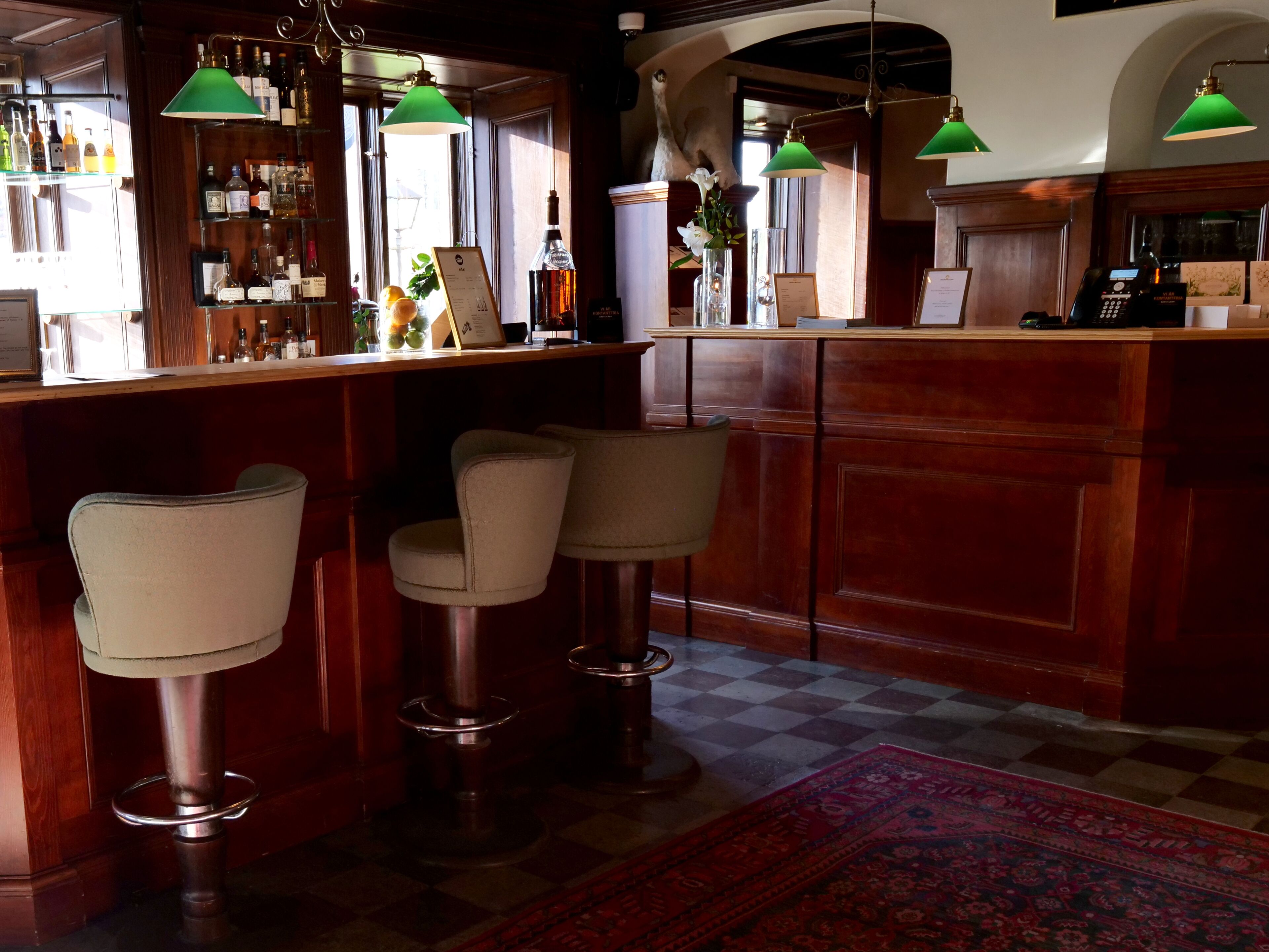 A bar area with wooden furniture, green pendant lights, and a checkered floor.