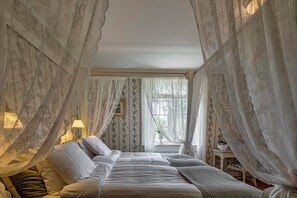A bedroom with a bed, a bedside table, a lamp, and sheer curtains.