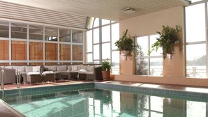 Une piscine intérieure aux murs carrelés, un espace détente avec des coussins et des plantes en pot.
