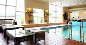 Una piscina interior con zona de estar, asientos y plantas en macetas.
