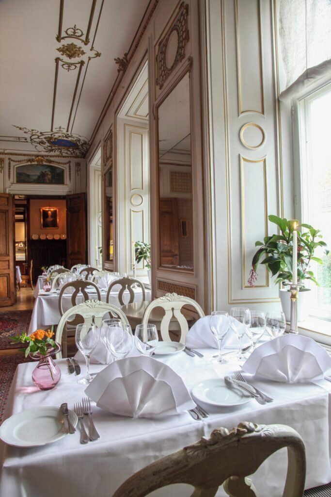 A dining area with tables set for a meal, featuring white tablecloths and elegant chairs.