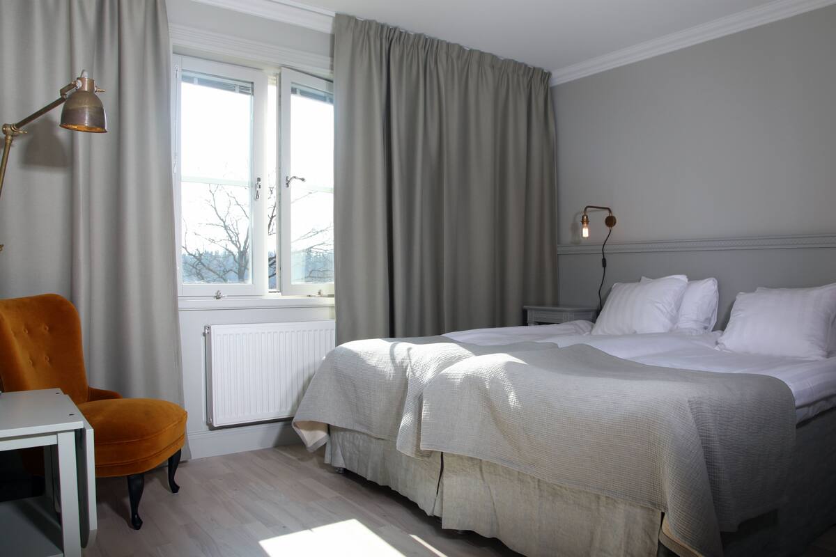 A hotel room with a bed, a chair, a table, and a window with curtains.