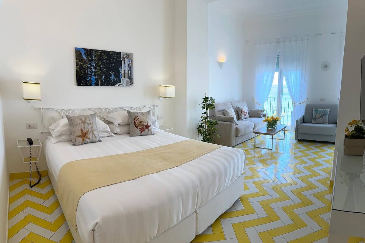 A hotel room with a large bed, a sofa, a coffee table, and a painting on the wall.