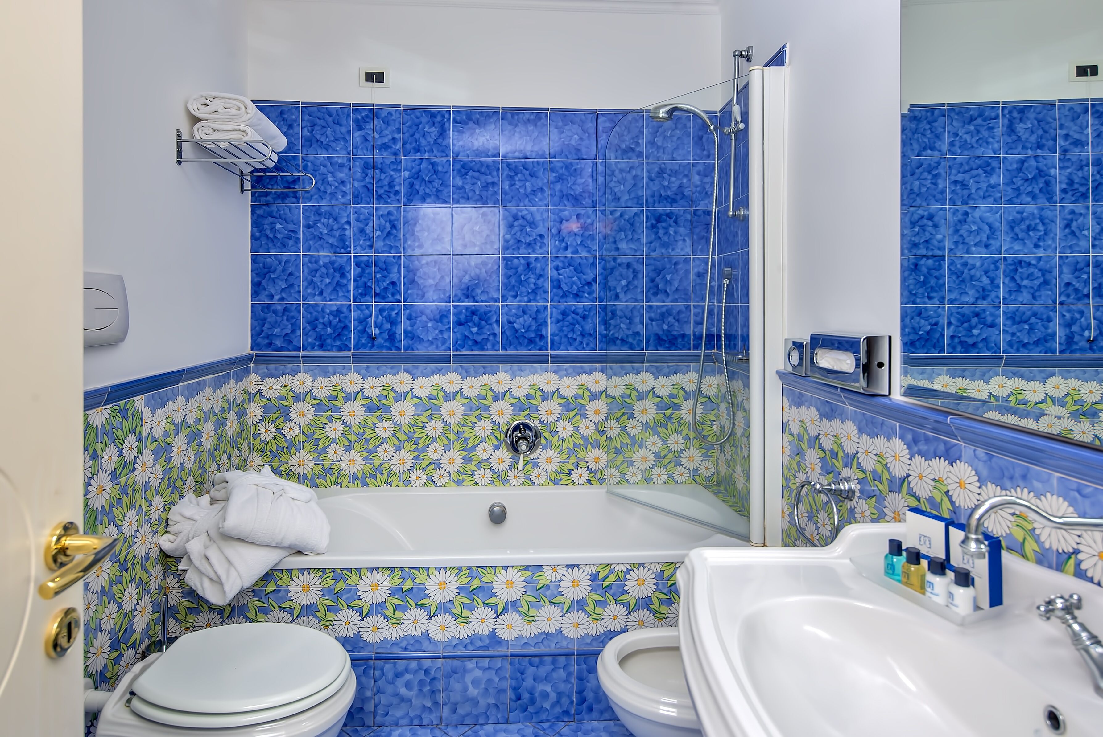Een badkamer met een bad, toilet en wastafel, met blauwe bloementegels en een handdoekhouder.