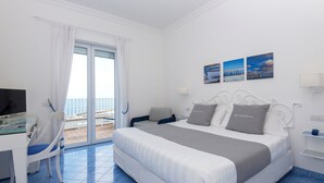 A hotel room with a bed, a desk, a chair, a balcony with a view, and a wall with three pictures.