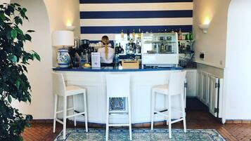Zona de bar con pared azul y blanca a rayas, una barra con caja registradora y dos taburetes blancos.