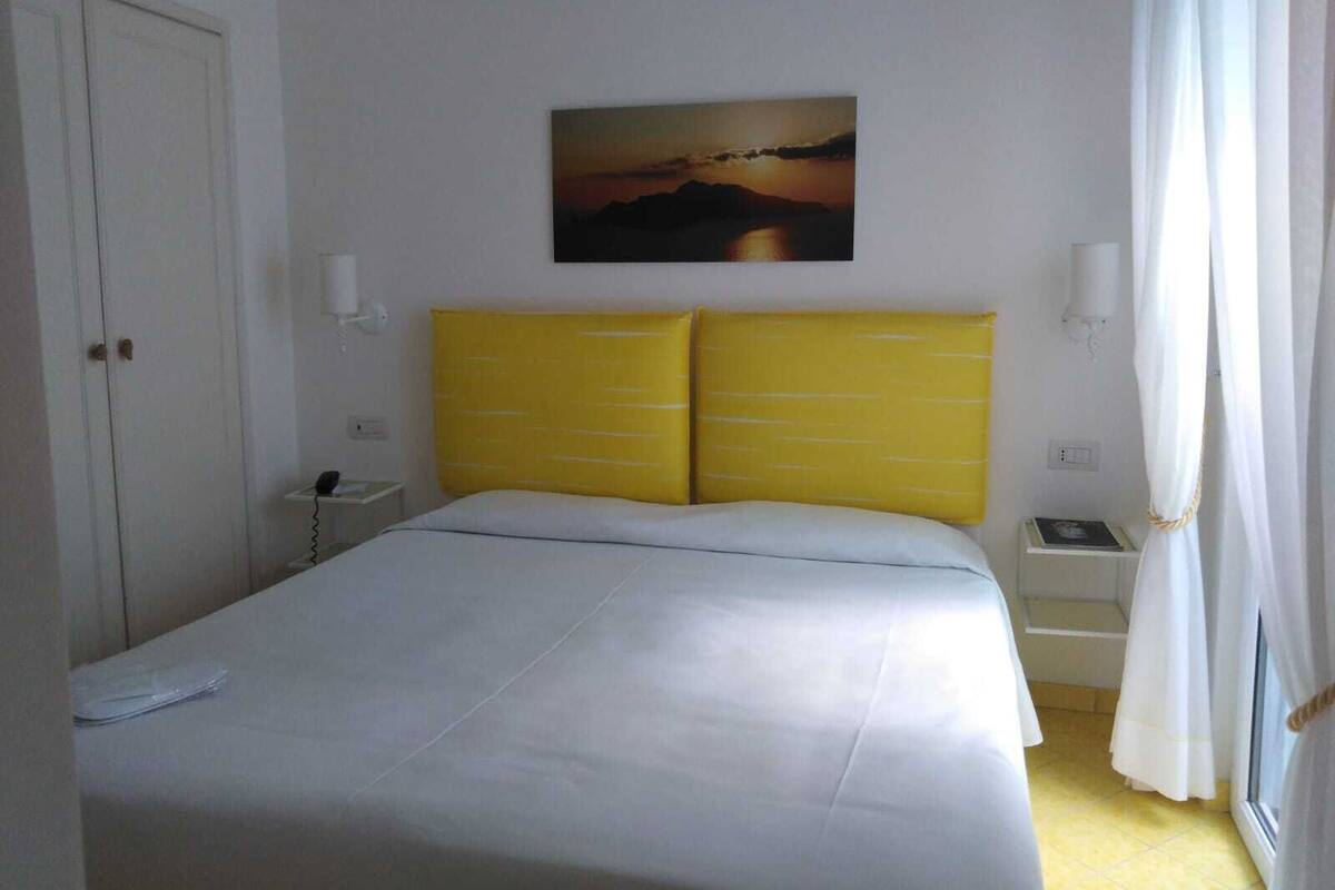 A bedroom with a bed, a nightstand, a lamp, and a painting on the wall.