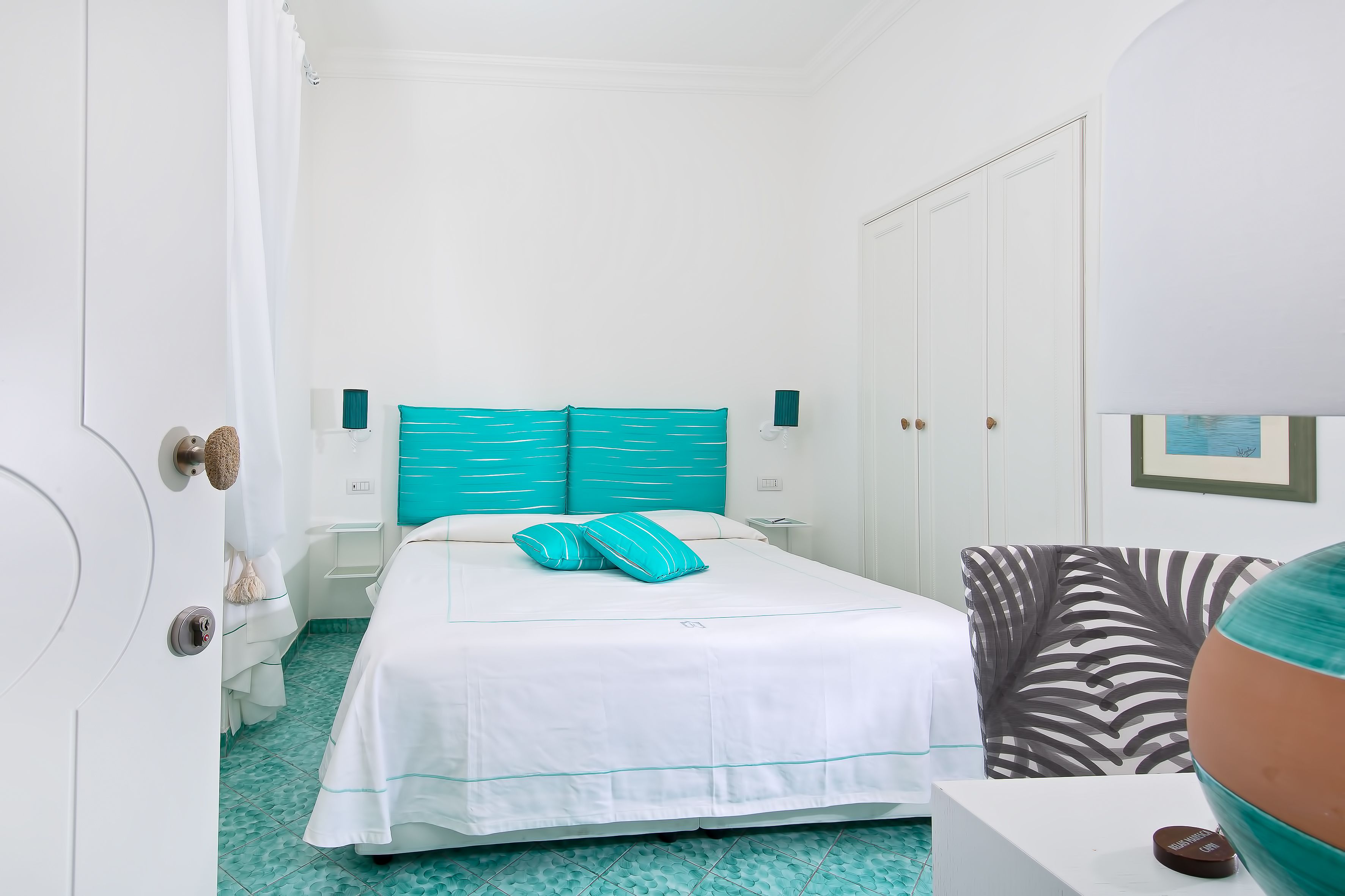 A hotel room with a bed, a chair, a desk, and a door.