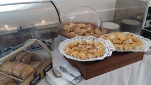 A buffet with various baked goods, including bread and pastries, displayed on a wooden board with a lace doily.