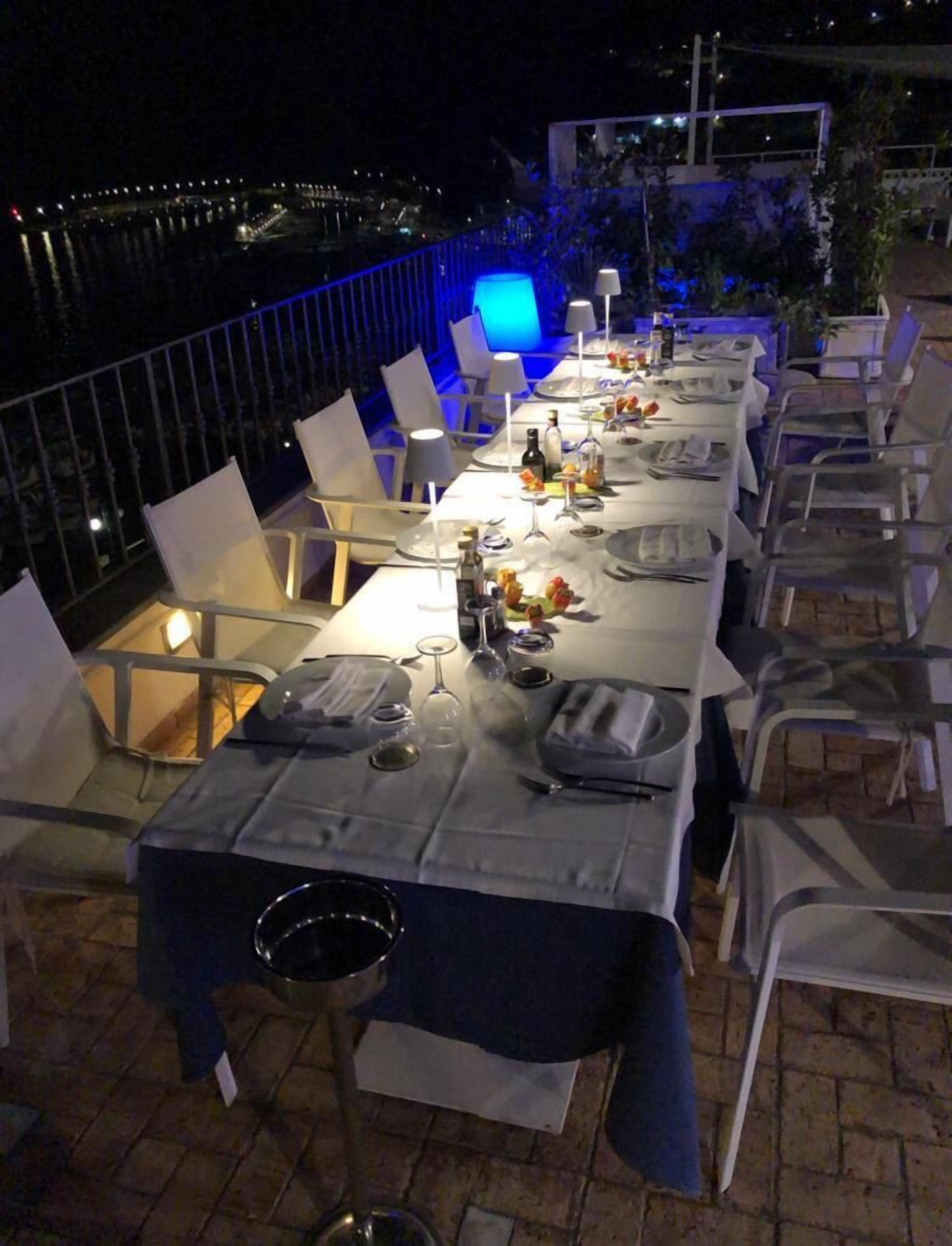 An outdoor dining area with tables set for a meal, chairs, and a view of the water.