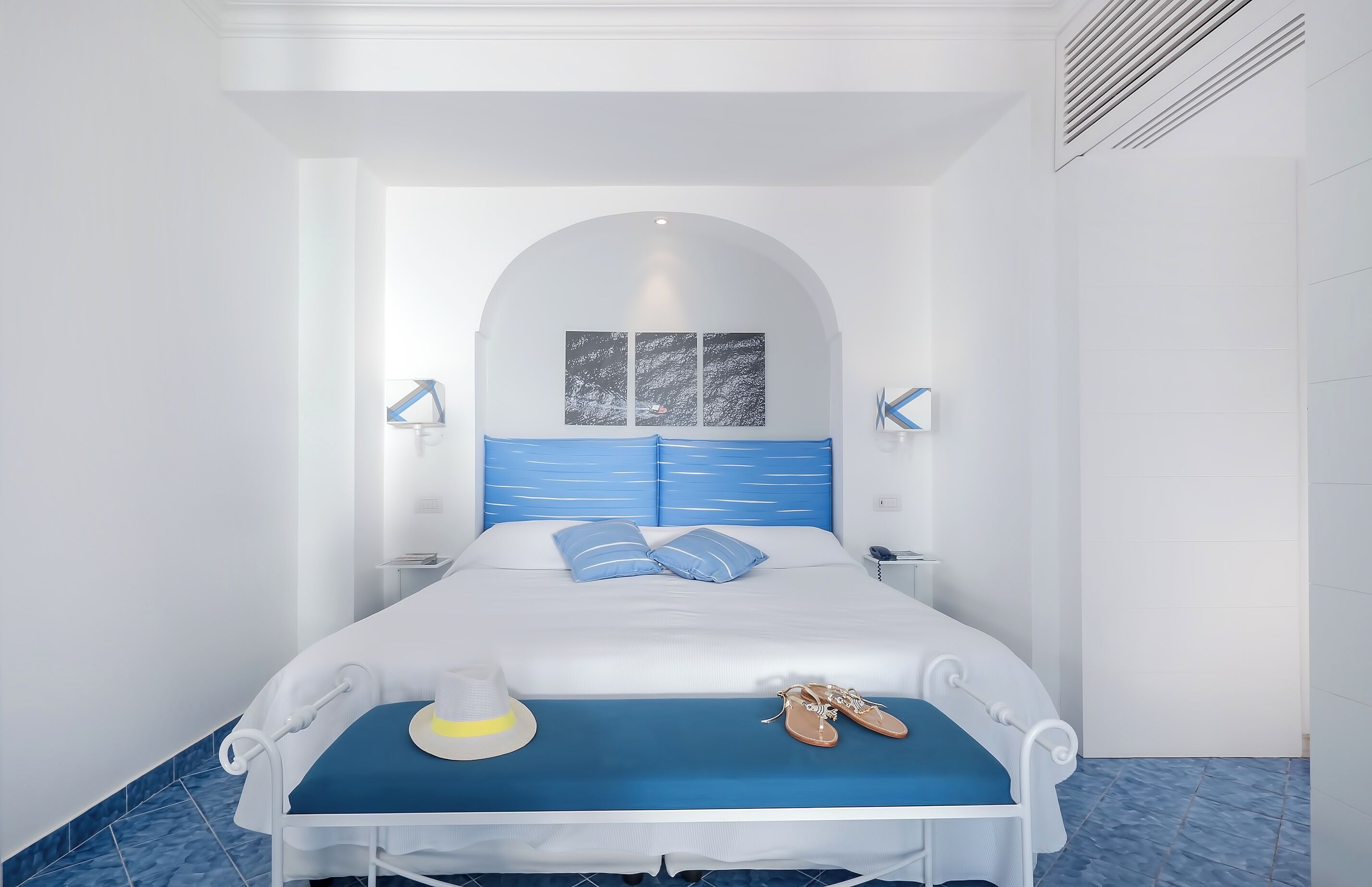 Een keurig opgemaakt hotelkamer met een bed, nachtkastjes, een hoed en schoenen op het bed.