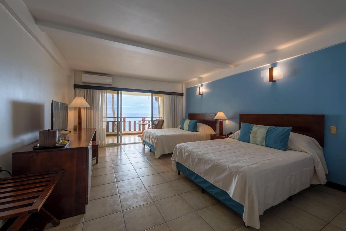 Une chambre d’hôtel avec deux lits, un bureau, une chaise et un balcon donnant sur la mer.