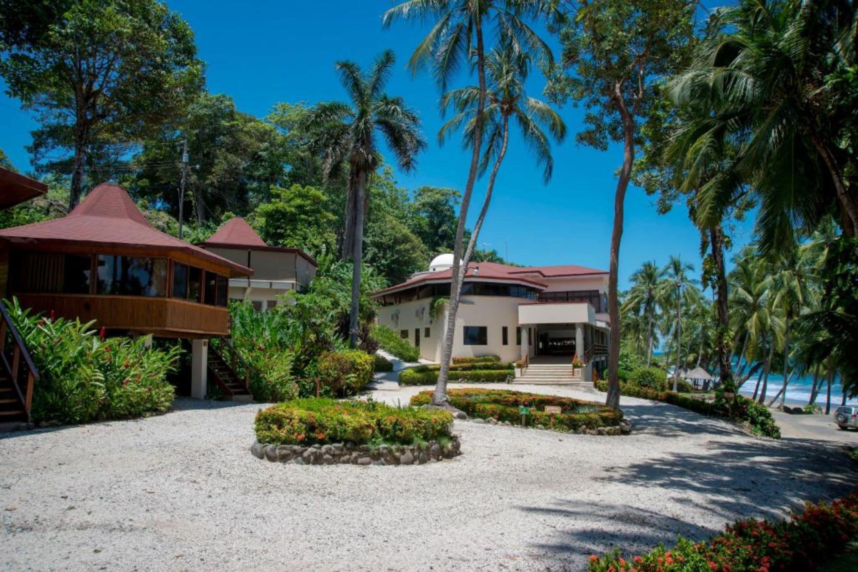 A resort with a covered outdoor area, palm trees, and a building with a red roof.