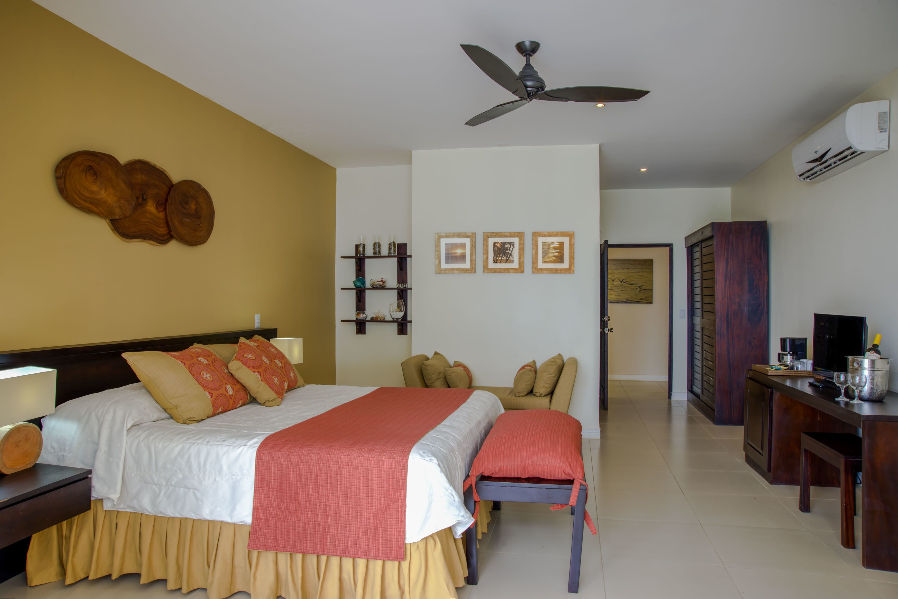 Une chambre d’hôtel comprenant un lit, des tables de chevet, un bureau, une chaise, un ventilateur de plafond et un climatiseur fixé au mur.