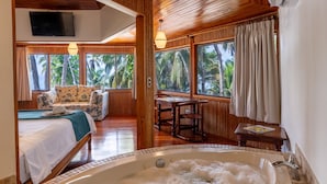 A room with a wooden ceiling, a bed, a sofa, a table, a chair, a window with curtains, and a bathtub.