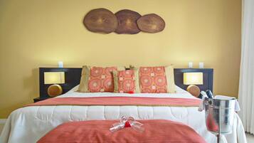 A hotel room with a bed, pillows, bedside lamps, a nightstand, and a bedside table with a lamp and a bottle.
