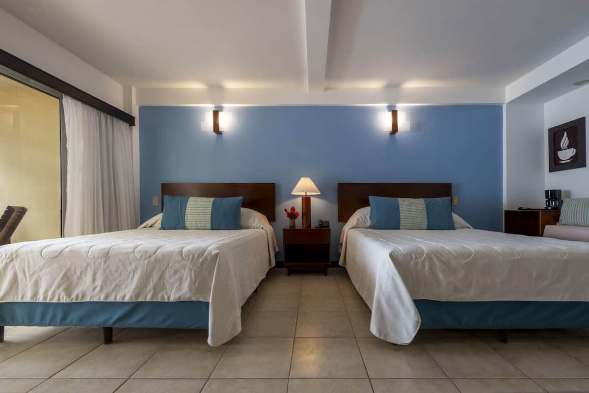 Une chambre d’hôtel avec deux lits, une table de chevet avec une lampe et un luminaire fixé au mur.
