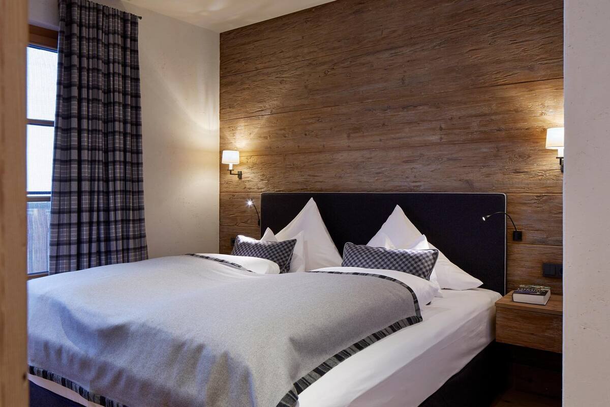 Ein Hotelzimmer mit einem großen Bett, einer Wand aus Holzpaneelen, zwei Nachttischlampen und einem Fenster mit Vorhängen.