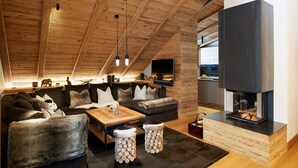 A cozy living room with a fireplace, wooden ceiling, and a sofa set. - Arlberg Hospiz Chalet Suiten (Sankt Anton am Arlberg)